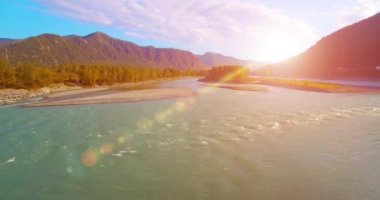 4k UHD hava görüntüsü. Güneşli yaz sabahında taze soğuk dağ nehri üzerinde alçak uçuş. Horisont 'ta yeşil ağaçlar ve güneş ışınları