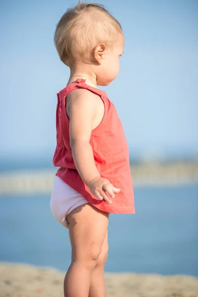 Bambina in abito rosso che gioca sulla spiaggia di sabbia vicino al mare . — Foto Stock