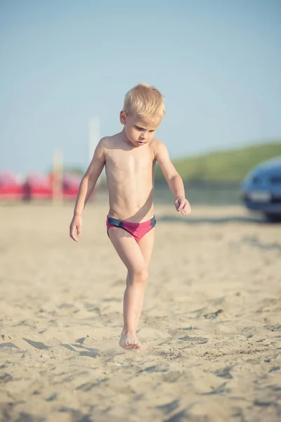 Ładny chłopczyk chodzenie na piaszczystej plaży w pobliżu morza. Na wybrzeżu Oceanu. — Zdjęcie stockowe