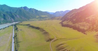 Güneşli yaz sabahında havadan kırsal dağ yolu ve çayır. Asfalt karayolu ve nehir.