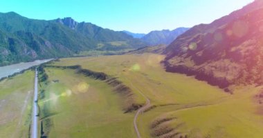 Güneşli yaz sabahında havadan kırsal dağ yolu ve çayır. Asfalt karayolu ve nehir.