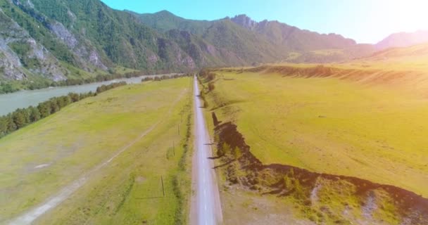 Luftlinie ländliche Bergstraße und Wiese an einem sonnigen Sommermorgen. Asphaltstraße und Fluss. — Stockvideo