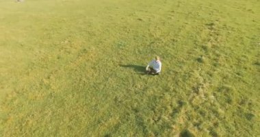 UHD 4k havadan görünümü. Defter pad ile yeşil çim sahasında oturan işadamı üzerinde düşük yörünge uçuş