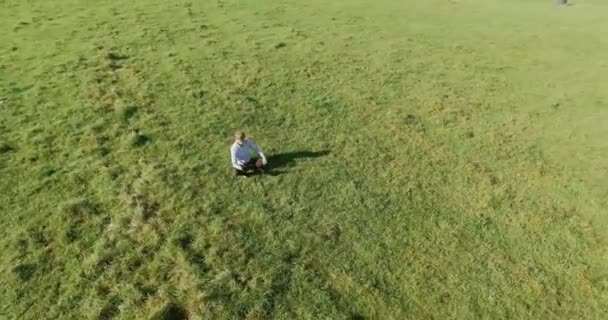 UHD 4k vue aérienne. Vol orbital bas au-dessus de l'homme d'affaires assis sur l'herbe verte avec bloc-notes au champ — Video
