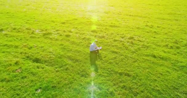 UHD 4k pandangan udara. Penerbangan orbital rendah di atas pengusaha duduk di rumput hijau dengan notebook pad di lapangan — Stok Video