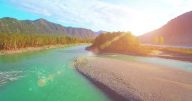 4k UHD hava görüntüsü. Güneşli yaz sabahında taze soğuk dağ nehri üzerinde alçak uçuş. Horisont 'ta yeşil ağaçlar ve güneş ışınları