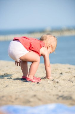Denize yakın kumlu plajda oynayan Kırmızı elbiseli kız bebek. 