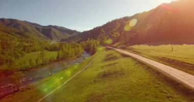 Güneşli yaz sabahında taze dağ nehri ve çayır üzerinde uçuşun ortasında. Aşağıdaki kırsal toprak yol.