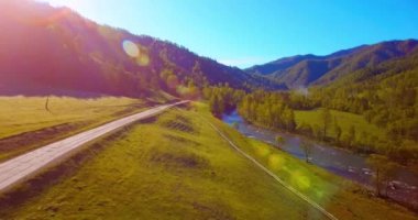 Güneşli yaz sabahında taze dağ nehri ve çayır üzerinde uçuşun ortasında. Aşağıdaki kırsal toprak yol.