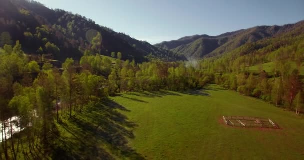 真夏の朝、新鮮な山の川や牧草地を上空で空中飛行します。下の未舗装道路. — ストック動画