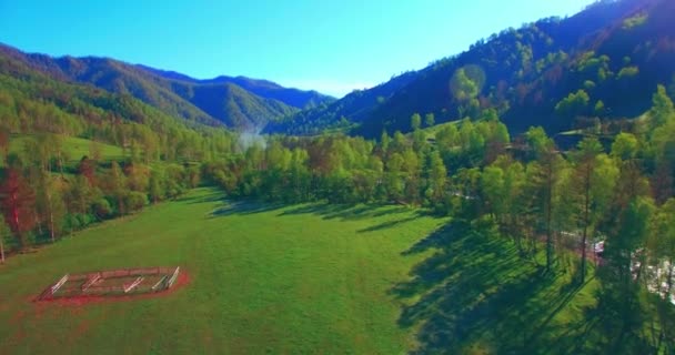 Mid air flight over fresh mountain river and meadow at sunny summer morning. Rural dirt road below. — Stock Video