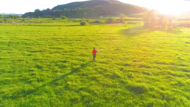 Vuelo sobre el hombre del deporte en el prado de hierba verde perfecto. Puesta de sol en montaña — Vídeo de stock