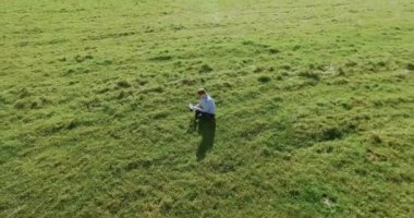 UHD 4k havadan görünümü. Defter pad ile yeşil çim sahasında oturan işadamı üzerinde düşük yörünge uçuş