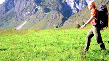 Sırt çantası ile yeşil dağ çayır üzerinde yürüyen adam hiking. Yaz spor ve eğlence kavramı.
