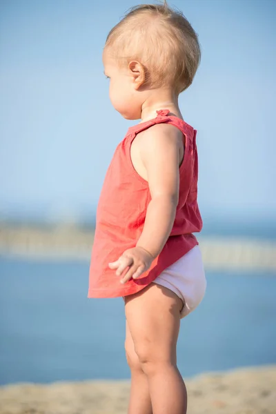 Niña en vestido rojo jugando en la playa de arena cerca del mar . —  Fotos de Stock