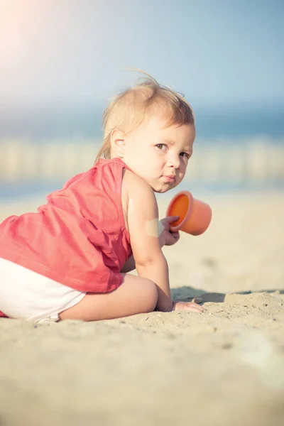 Bambina in abito rosso che gioca sulla spiaggia di sabbia vicino al mare . — Foto Stock