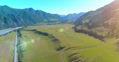 Güneşli yaz sabahında havadan kırsal dağ yolu ve çayır. Asfalt karayolu ve nehir.