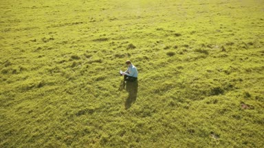 UHD 4k havadan görünümü. Defter pad ile yeşil çim sahasında oturan işadamı üzerinde düşük yörünge uçuş
