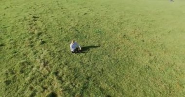 UHD 4k havadan görünümü. Defter pad ile yeşil çim sahasında oturan işadamı üzerinde düşük yörünge uçuş