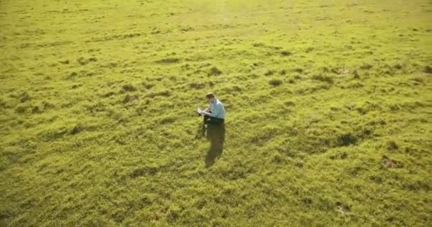 UHD 4k vue aérienne. Vol orbital bas au-dessus de l'homme d'affaires assis sur l'herbe verte avec bloc-notes au champ — Video