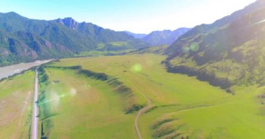 Güneşli yaz sabahında havadan kırsal dağ yolu ve çayır. Asfalt karayolu ve nehir.