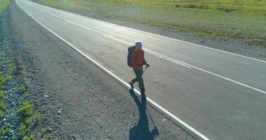 Asfalt yolda yürüyen otostopçu turist üzerinden uçuş. Yaz günü büyük bir kırsal vadi. Sırt çantalı gezgin..