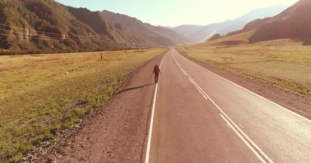 アスファルトの道路を歩くヒッチハイカーの観光客の上のフライト。夏の日に巨大な田舎の谷。リュックハイキング男. — ストック動画