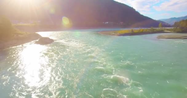 Vol à basse altitude au-dessus d'une rivière de montagne fraîche et rapide avec des rochers au soleil matin d'été. — Video