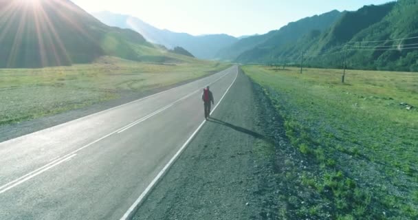 Volo sopra autostoppista turistico a piedi su strada asfaltata. Enorme valle rurale durante la giornata estiva. Zaino escursionista ragazzo. — Video Stock