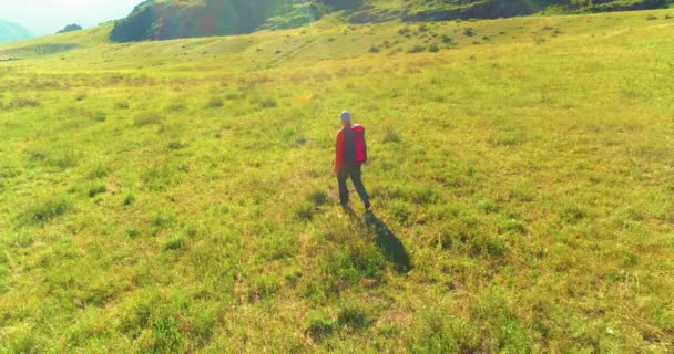 Terbang di atas Backpack hiking turis berjalan melintasi lapangan gunung hijau. Besar lembah pedesaan pada hari musim panas. — Stok Video