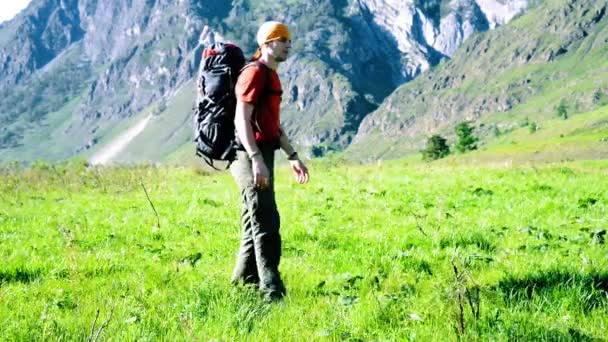 Sırt çantası ile yeşil dağ çayır üzerinde yürüyen adam hiking. Yaz spor ve eğlence kavramı. — Stok video