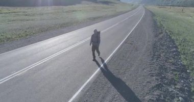 Asfalt yolda yürüyen otostopçu turist üzerinden uçuş. Yaz günü büyük bir kırsal vadi. Sırt çantalı gezgin..