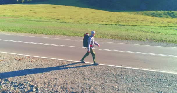 Volo sopra autostoppista turistico a piedi su strada asfaltata. Enorme valle rurale durante la giornata estiva. Zaino escursionista ragazzo. — Video Stock