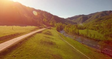 Güneşli yaz sabahında taze dağ nehri ve çayır üzerinde uçuşun ortasında. Aşağıdaki kırsal toprak yol.