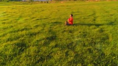 Yeşil çimlerde spor yogacısı üzerinde alçak irtifa radyal uçuş. Dağda gün batımı.