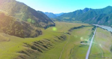 Güneşli yaz sabahında havadan kırsal dağ yolu ve çayır. Asfalt karayolu ve nehir.