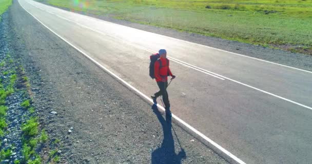 アスファルトの道路を歩くヒッチハイカーの観光客の上のフライト。夏の日に巨大な田舎の谷。リュックハイキング男. — ストック動画