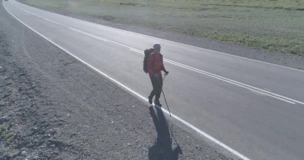 アスファルトの道路を歩くヒッチハイカーの観光客の上のフライト。夏の日に巨大な田舎の谷。リュックハイキング男. — ストック動画