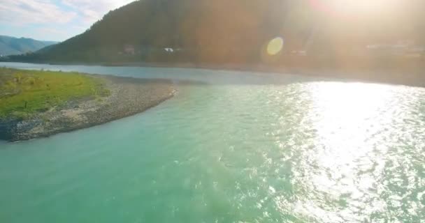 Vol à basse altitude au-dessus d'une rivière de montagne fraîche et rapide avec des rochers au soleil matin d'été. — Video