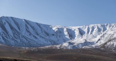 Güneşin kar dağının tepesinde kristal berrak gökyüzünde hareketinin zamanı. Sonbahar otlağında sarı çimenler. Vahşi sonsuz doğa..