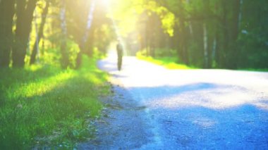Asfalt yolda koşan sporcu. Kırsal şehir parkı. Yeşil ağaç ormanı ve ufukta güneş ışığı.