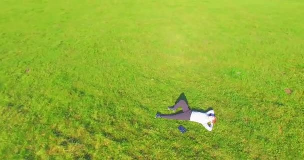 Low orbital flight around man on green grass with notebook pad at yellow rural field. — Stock Video