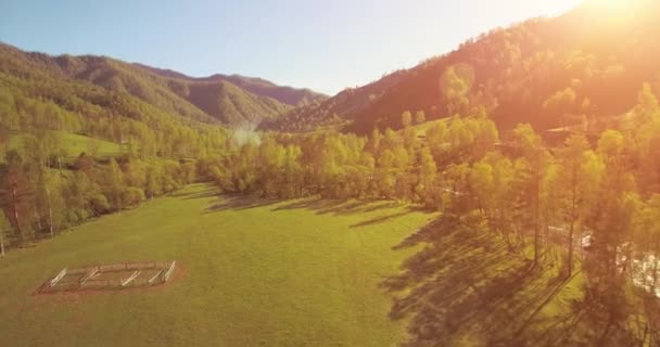 Mid air flight over fresh mountain river and meadow at sunny summer morning. Rural dirt road below. — Stock Video