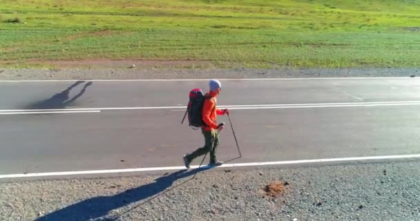 Volo sopra autostoppista turistico a piedi su strada asfaltata. Enorme valle rurale durante la giornata estiva. Zaino escursionista ragazzo. — Video Stock