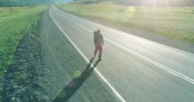 Asfalt yolda yürüyen otostopçu turist üzerinden uçuş. Yaz günü büyük bir kırsal vadi. Sırt çantalı gezgin..