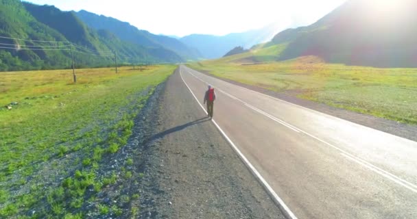 Vuelo sobre autoestopista turista caminando por carretera asfaltada. Gran valle rural en el día de verano. Mochila senderismo chico. — Vídeo de stock