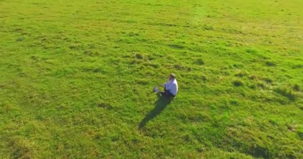 Vol orbital bas autour de l'homme sur herbe verte avec bloc-notes au champ rural jaune. — Video