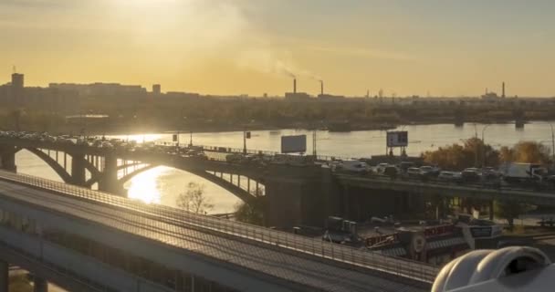 A városi élet időrendje. Napsugarak, kék ég, folyó és híd a horizonton. Közlekedési dugó nyári napnyugtakor. Motoros csúszómozgás — Stock videók