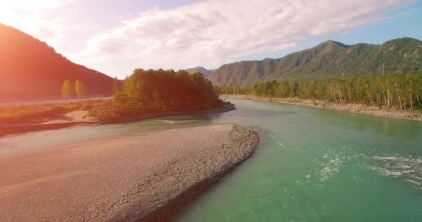 4k UHD aerial view. Low flight over fresh cold mountain river at sunny summer morning. Green trees and sun rays on horisont — Stock Video