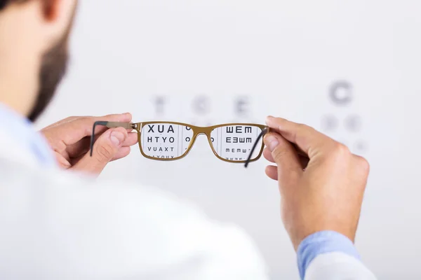 Opticien houdt bril tegenover gezichtsvermogen test-chart — Stockfoto